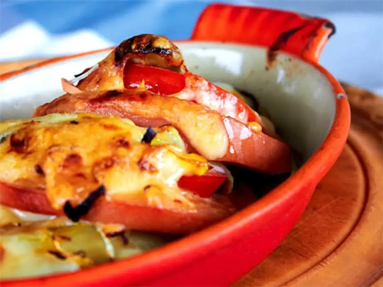 Baked falukorv with melted cheese and tomatoes in a red dish.