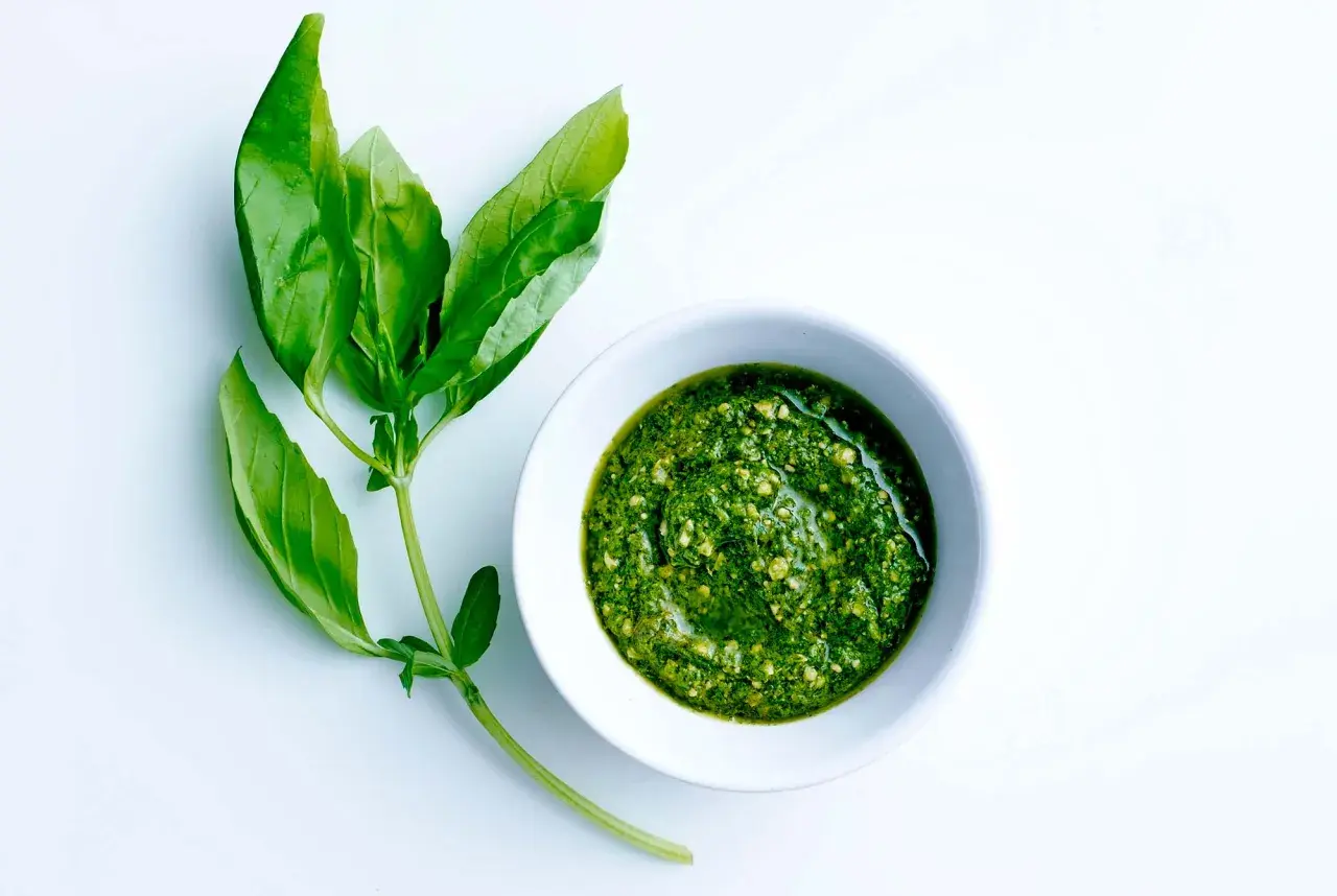 En skål med hemgjord egen pesto bredvid färska basilikablad.
