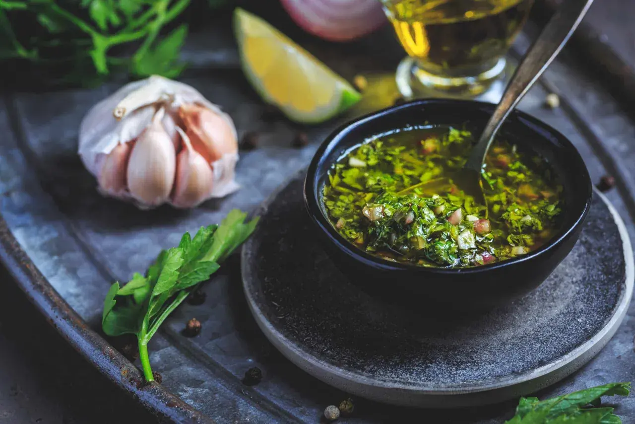 En skål med färsk chimichurri, redo att förhöja din nästa måltid. Ingredienser som vitlök, persilja och citron syns i närheten.