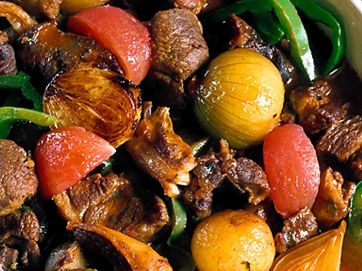 En mustig lammgryta med ben, full av möra köttbitar, gyllene lök, tomater och gröna paprikastrimlor.
