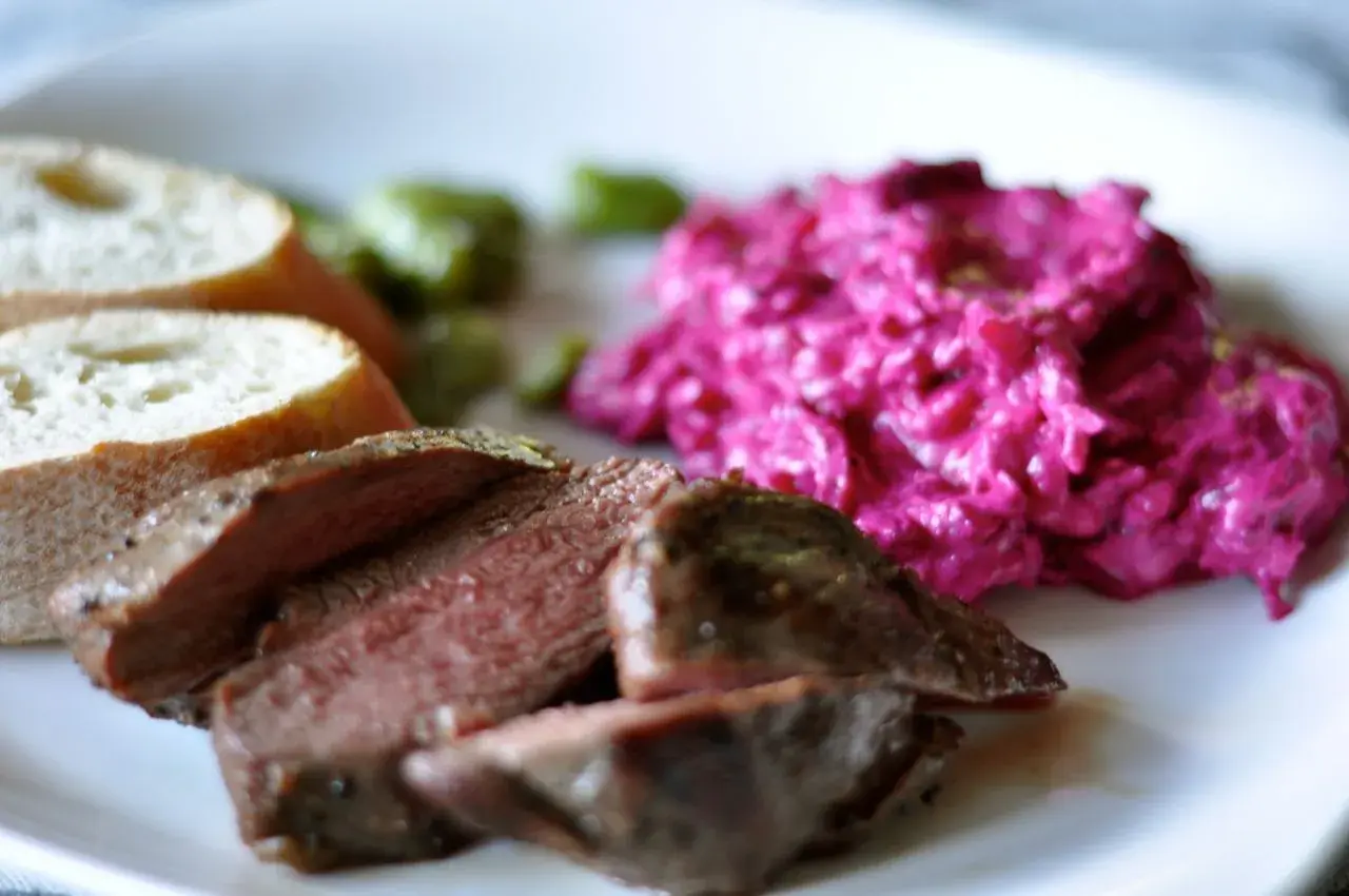 Skivad lammrostbiff med perfekt innertemp, serverad med rödbetssallad och bröd.