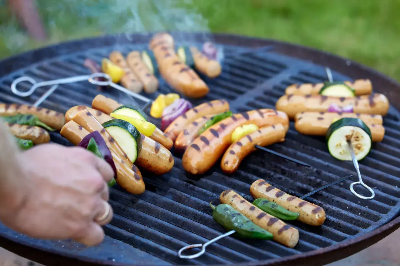 Grilla korv med grönsaker på en kolgrill. Röken stiger och ger en härlig doft.