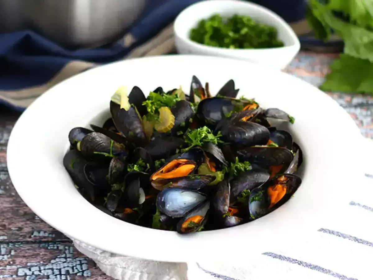 En skål med ångade musslor, moules marinières, garnerade med färsk persilja och serverade med en sidokål.