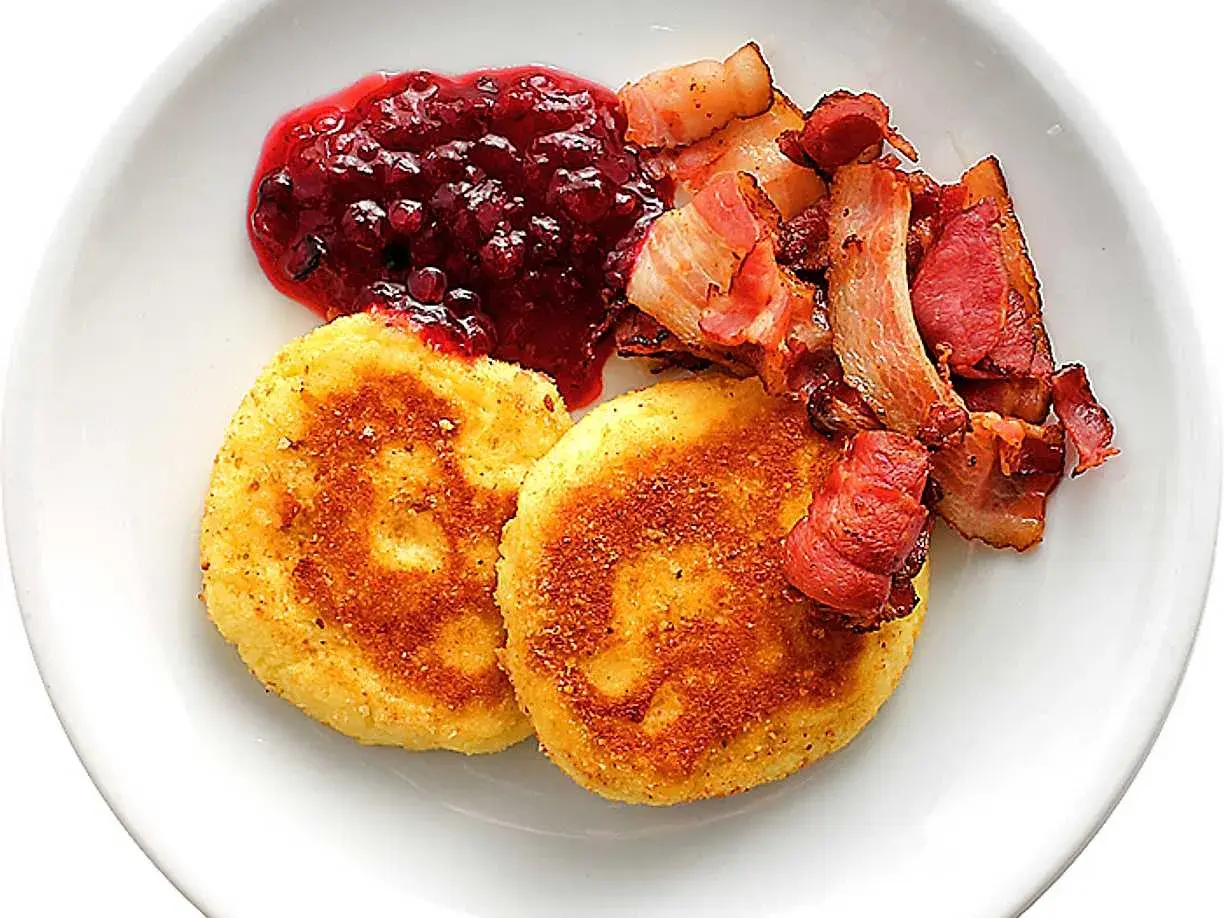Två gyllene potatisbullar airfryer serveras med rårörda lingon och knaperstekt bacon.