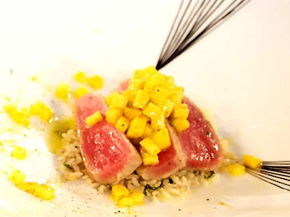 Röda skivor av tonfisk med tärnad mango ovanpå, serverade på ris. En utsökt kombination av tonfisk och mango.