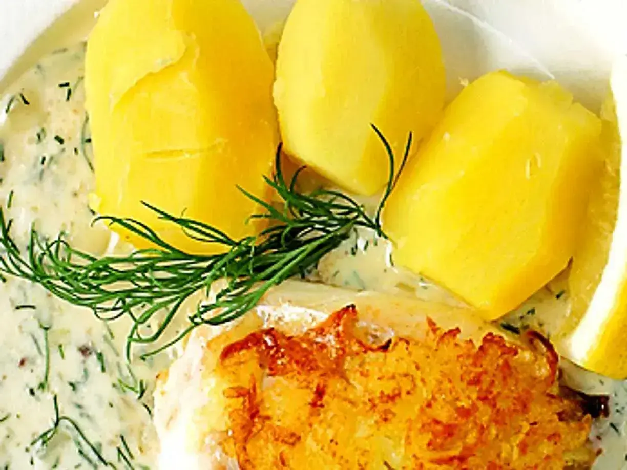 En portion med kokt potatis, en bit stekt fisk och en generös klick varm dillsås. Garnerat med färsk dill och en citronskiva.