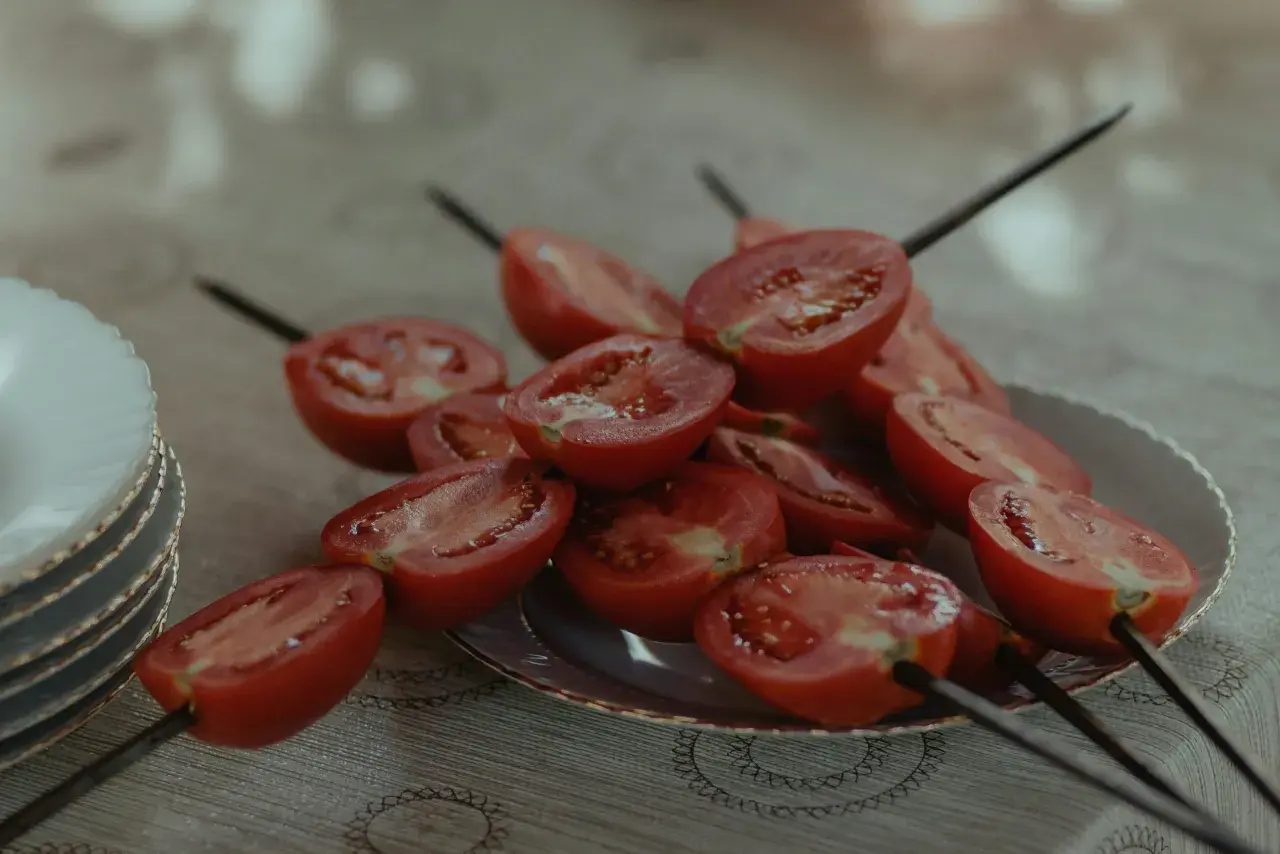 Halverade tomater på spett, redo för grillen. En stapel tallrikar syns till vänster.
