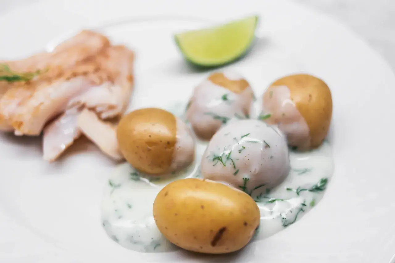 En tallrik med stuvad potatis, fisk och en limeklyfta. Potatisen är krämig och toppad med dill.
