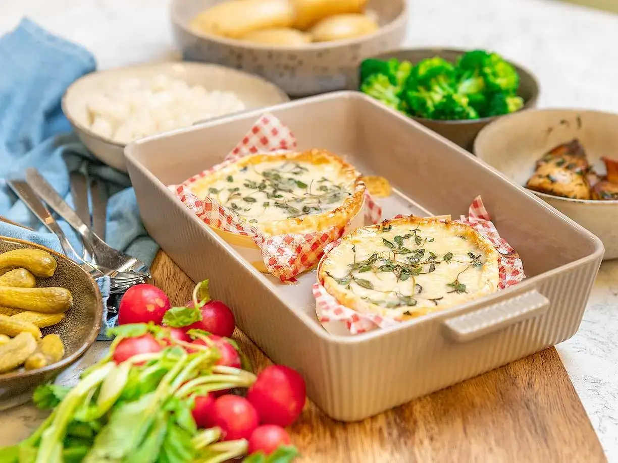 Två runda camembertostar i ugn, toppade med örter, serveras med rädisor, cornichoner och broccoli.