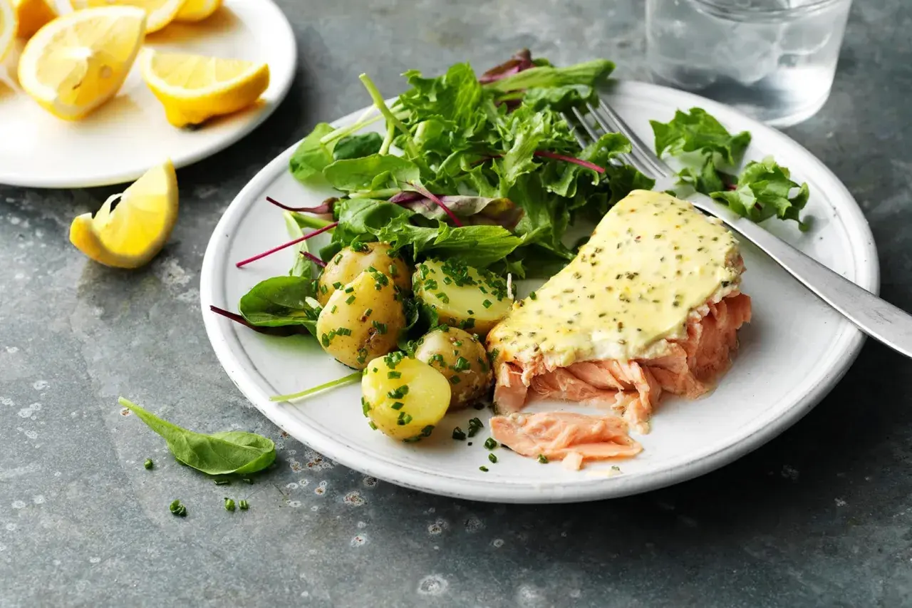 En tallrik med pulled lax, potatis och sallad. En citronskiva ligger bredvid.