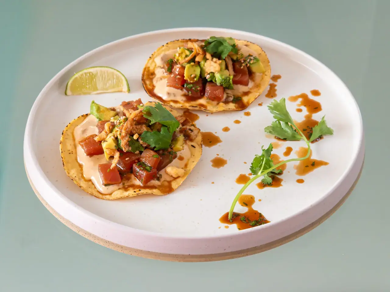 Två läckra tostadas med tonfisk tartar och avocado, toppade med koriander och en krämig sås. En limeklyfta ligger bredvid.