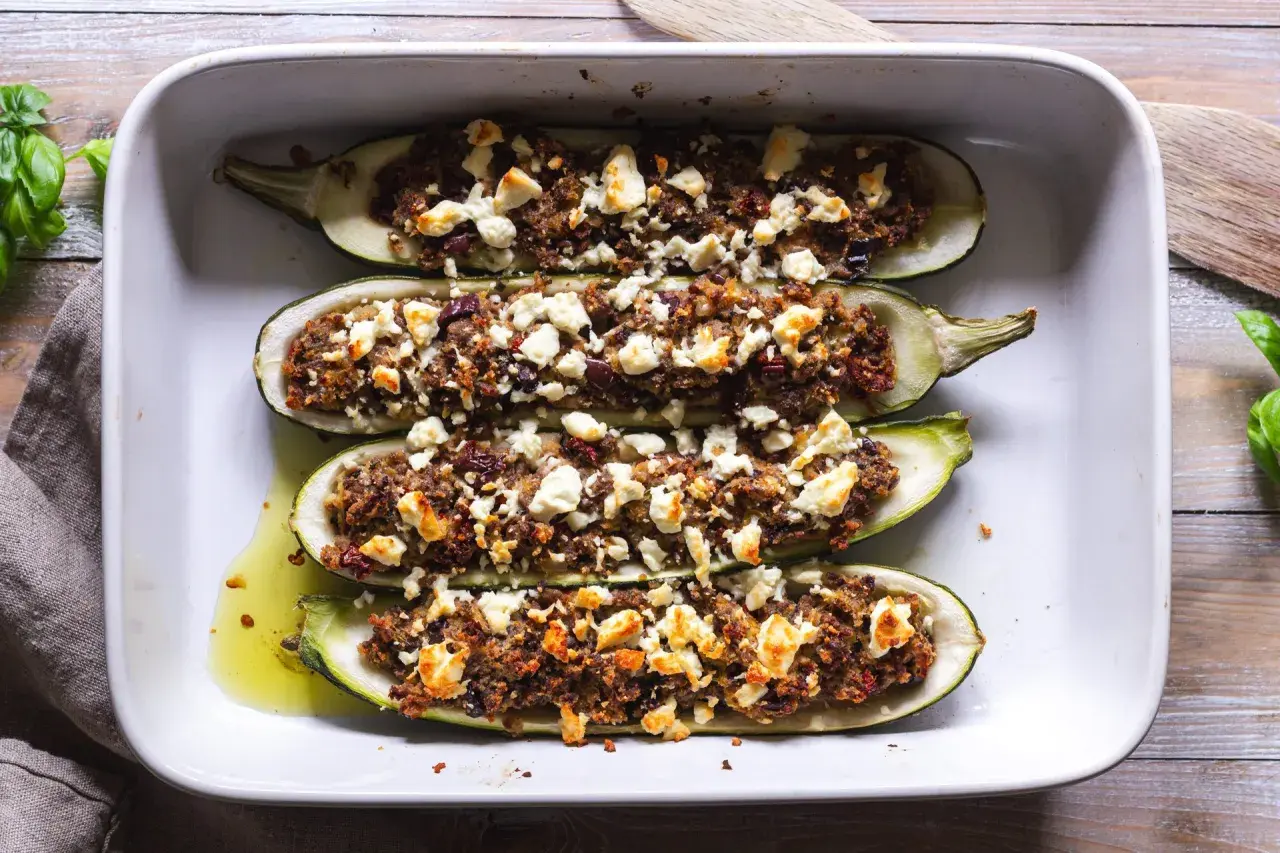 Fyra halverade zucchinis fyllda med en smakrik blandning och toppade med fetaost, redo att avnjutas som gratinerad zucchini.