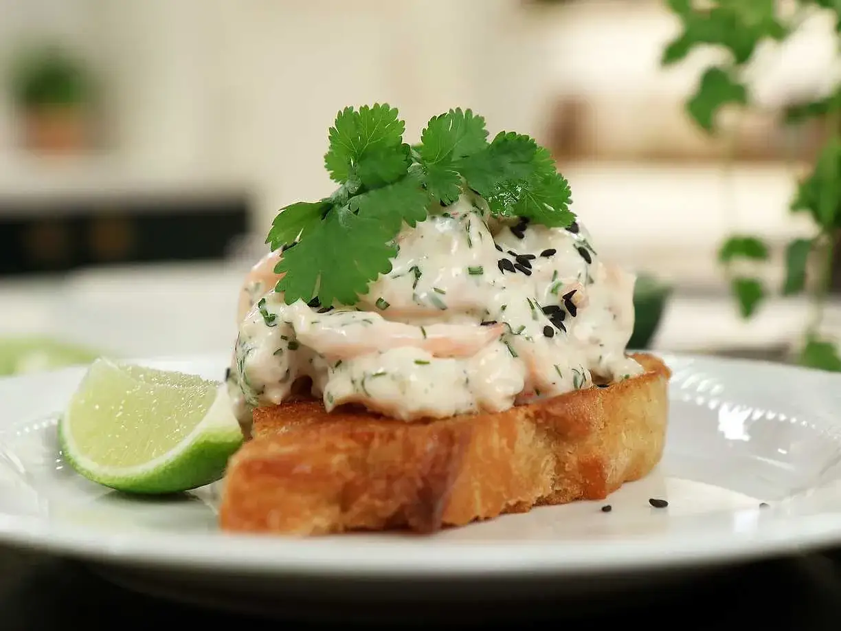 En rostad brödskiva toppad med krämig skagenröra, färska örter, svarta sesamfrön och en limeklyfta. En spännande asiatisk skagen-twist.