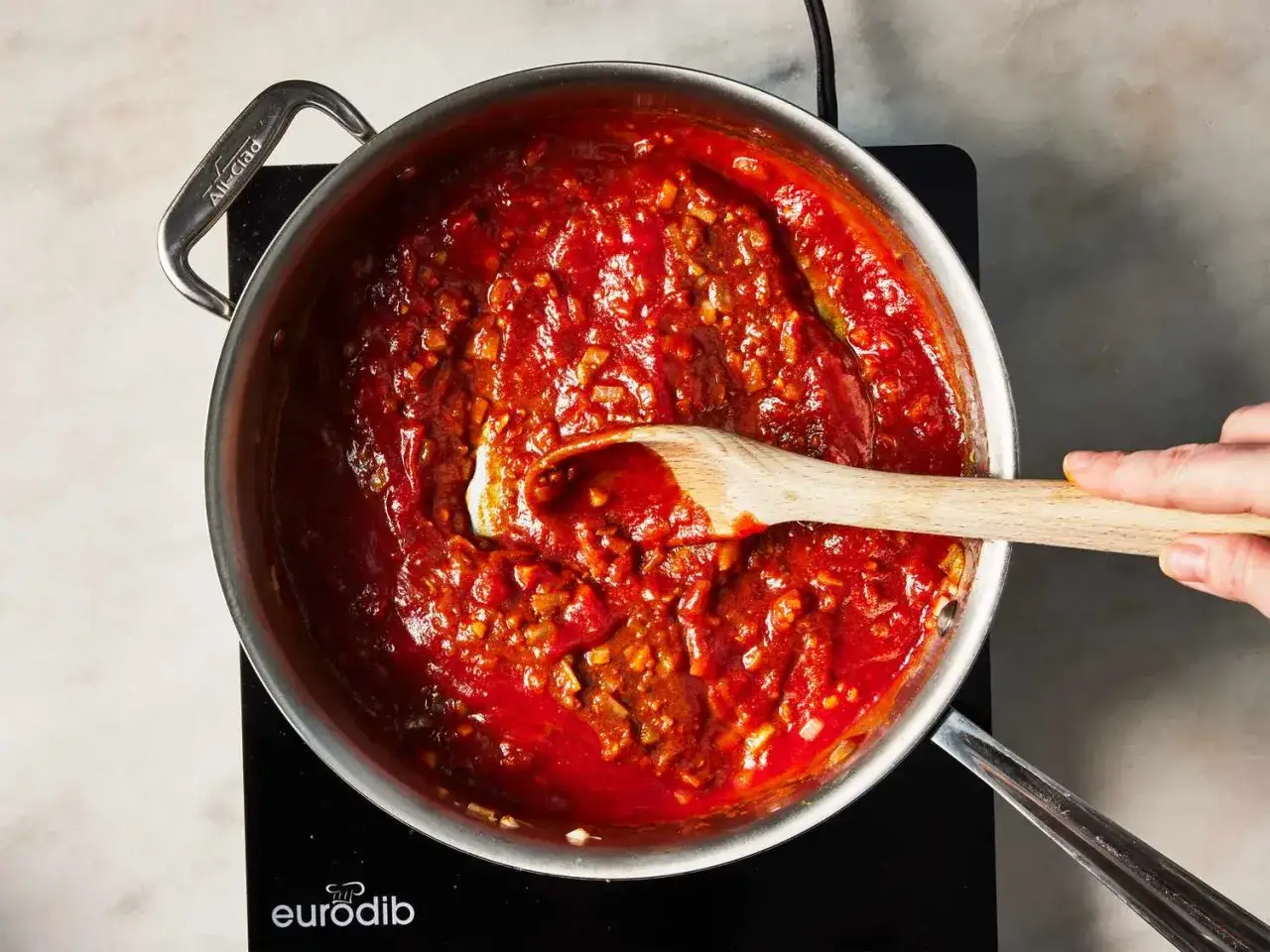 En hand r&ouml;r i en kastrull med en kr&auml;mig, r&ouml;d tikka masala s&aring;s.