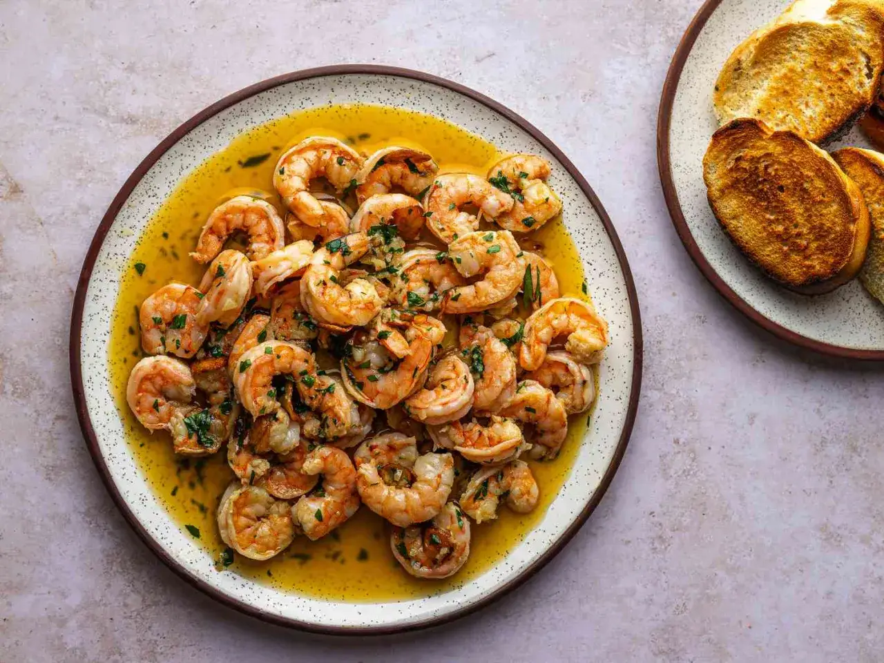 En tallrik med saftiga gambas pil pil i en gyllene olja, toppad med f&auml;rsk persilja. Bredvid syns rostat br&ouml;d.