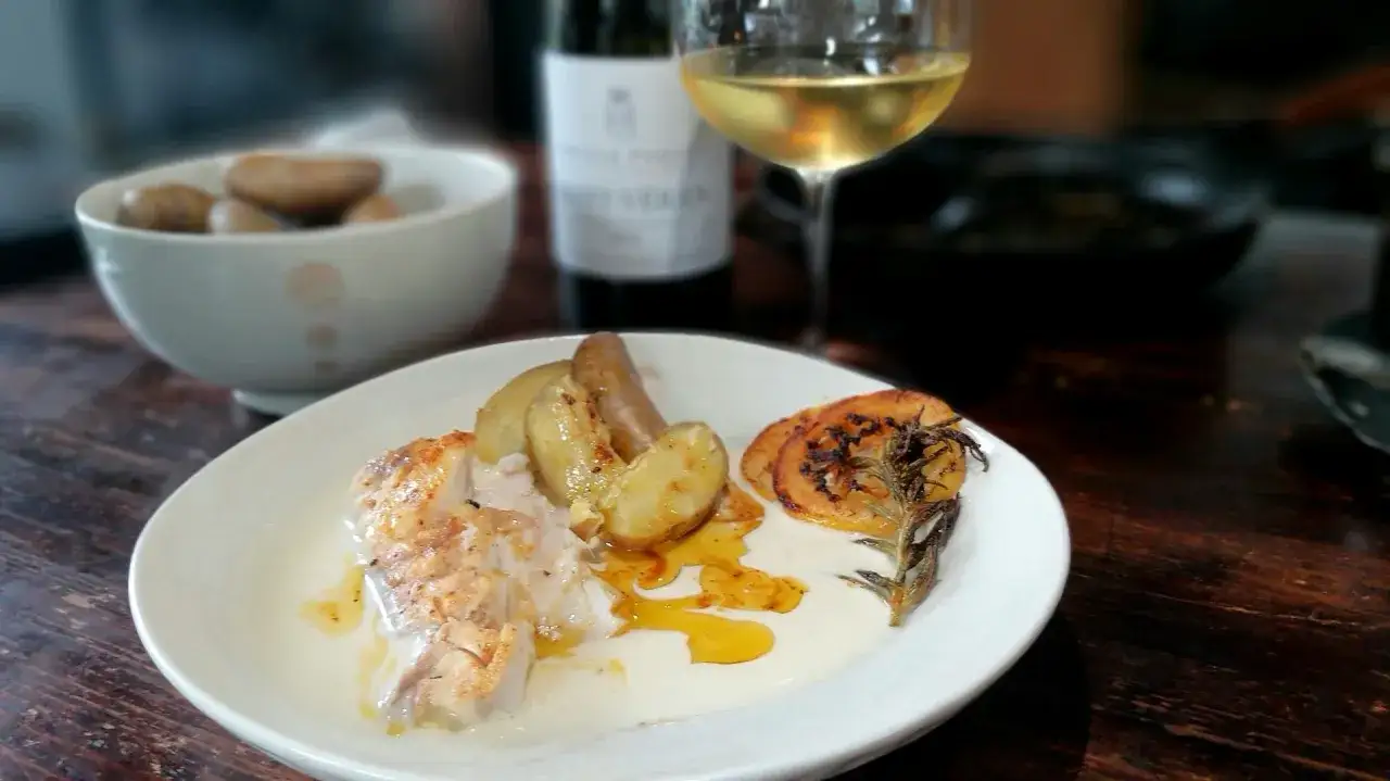 En tallrik med marulk, potatis och citron. Ett glas vitt vin och en flaska i bakgrunden. Ett enkelt marulk recept.