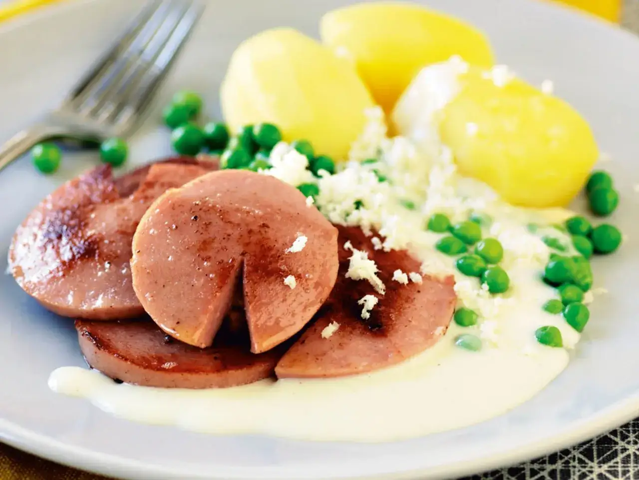 En tallrik med kokt falukorv med pepparrotss&aring;s, potatis och gr&ouml;na &auml;rtor.