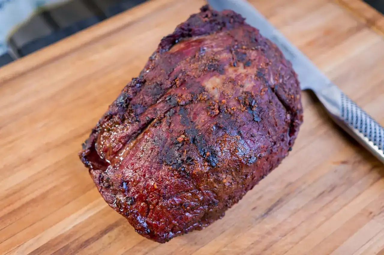 En saftig grillad rostbiff med en härlig yta, redo att skäras upp på en träskärbräda bredvid en kniv.