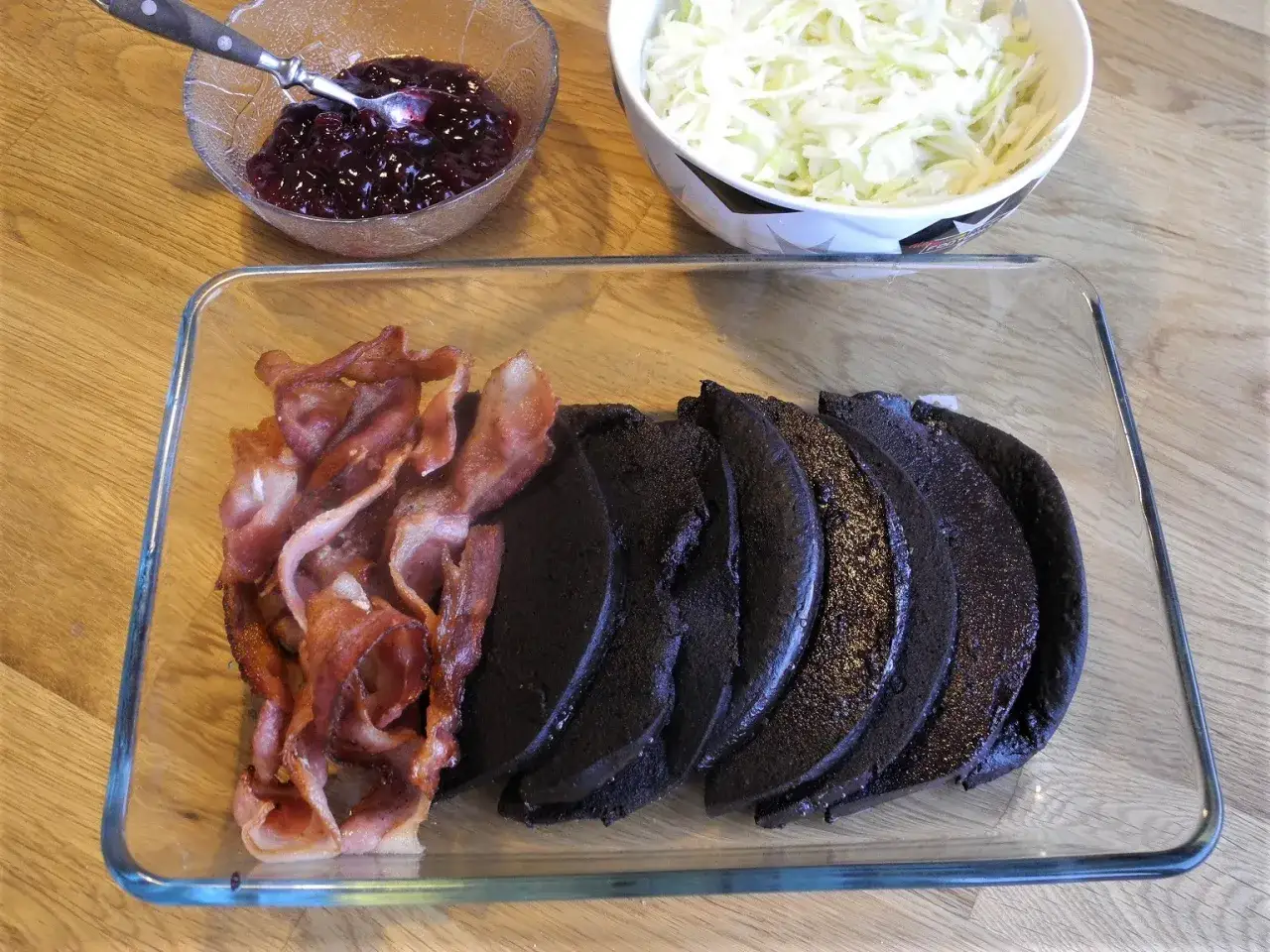 Skivor av blodpudding ligger redo att stekas bredvid knaperstekt bacon. Lingonsylt och vitk&aring;lssallad v&auml;ntar.