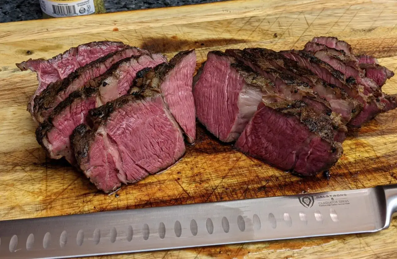 Perfekt tillagad rostbiff sous vide, skuren i saftiga skivor p&aring; en sk&auml;rbr&auml;da. Kniven ligger redo f&ouml;r mer.