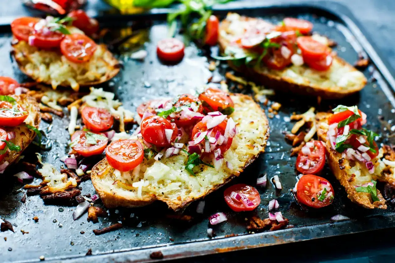 Romantiska tomater toppar krispiga bruschettas med smält ost och färska örter, serverade på en plåt.