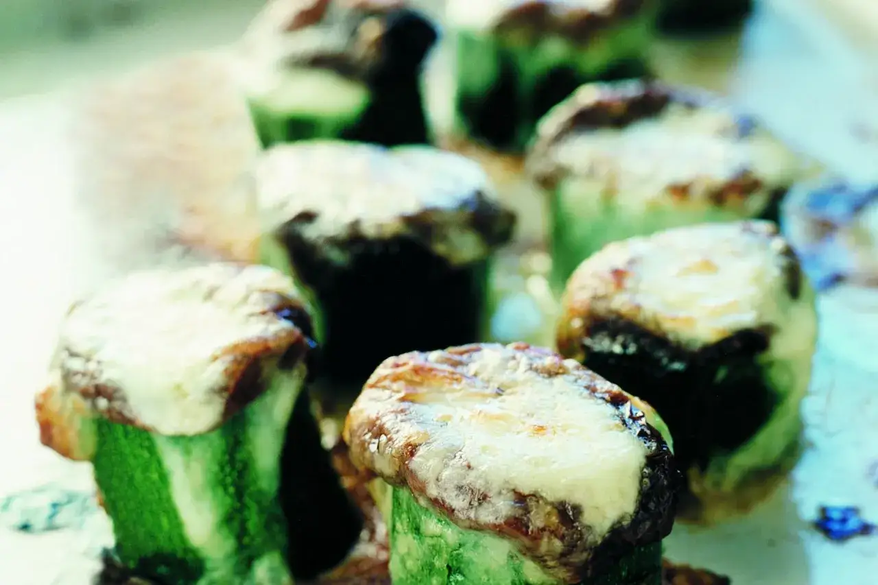 Små, runda bitar av gratinerad zucchini med smält ost och gyllene yta. En läcker och enkel rätt.