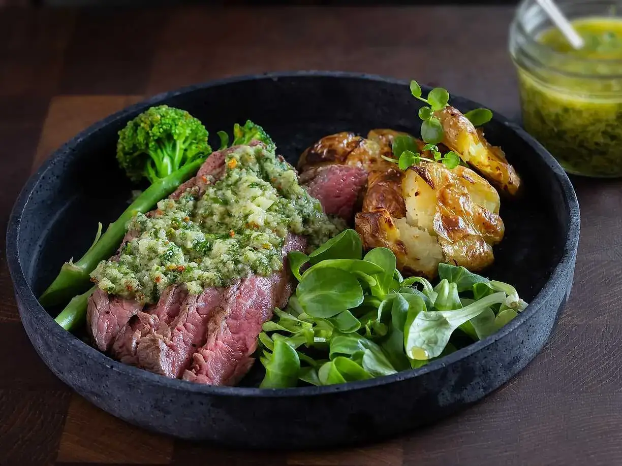 Skivad flankstek med chimichurri, serverad med rostade potatisar, broccoli och sallad.