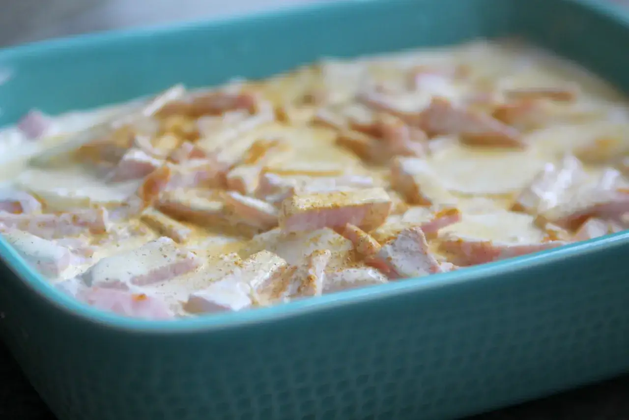 En grat&auml;ng med kassler och potatis i en turkos form, redo f&ouml;r ugnen. Ett klassiskt recept p&aring; kasslergrat&auml;ng.