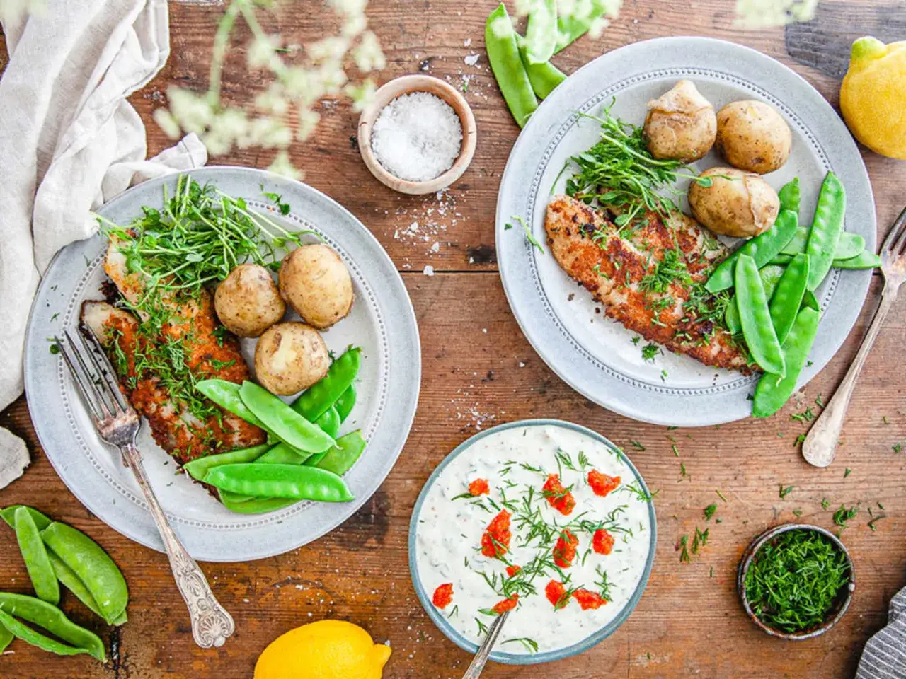 Två tallrikar med panerad abborre, småpotatis och sockerärtor. En skål med romsås och en skål med dill. Ett perfekt abborre recept för en härlig middag.