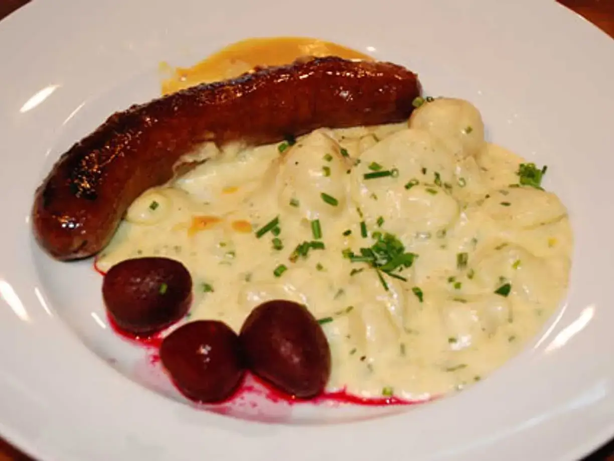 En korv med stuvad potatis, r&ouml;dbetor och en gul s&aring;s.