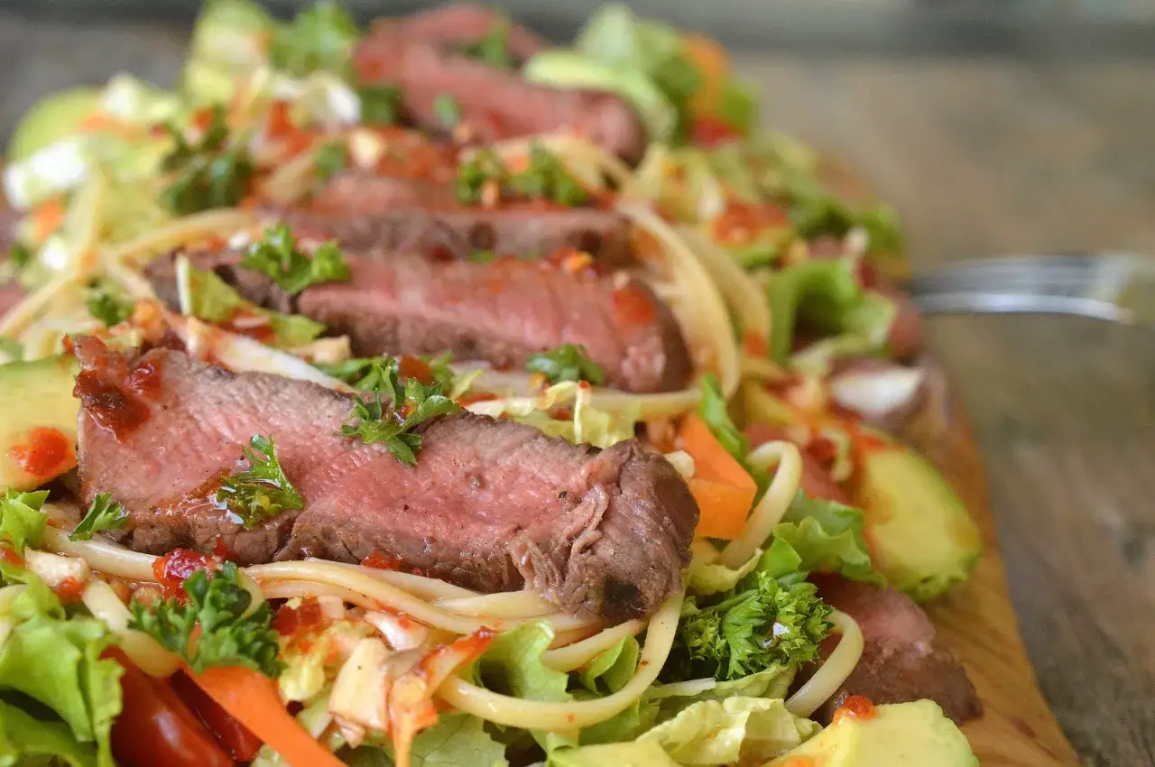 Skivad asiatisk ryggbiff serveras med nudlar, avokado, sallad och mor&ouml;tter.