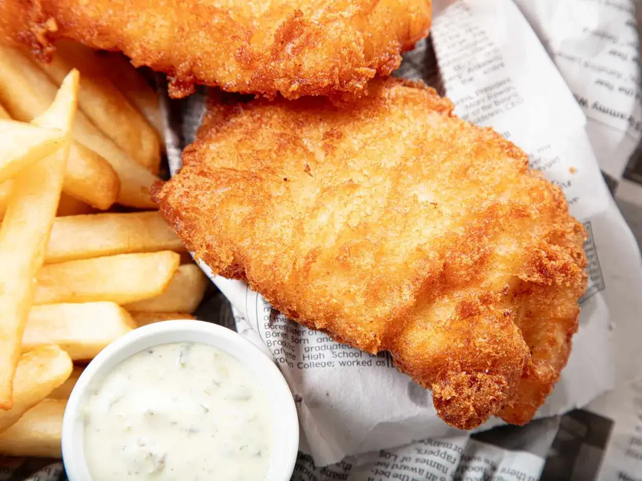 Krispigt friterad fisk och gyllene pommes frites, en klassisk fish and chips-rätt, serveras med en krämig dippsås.