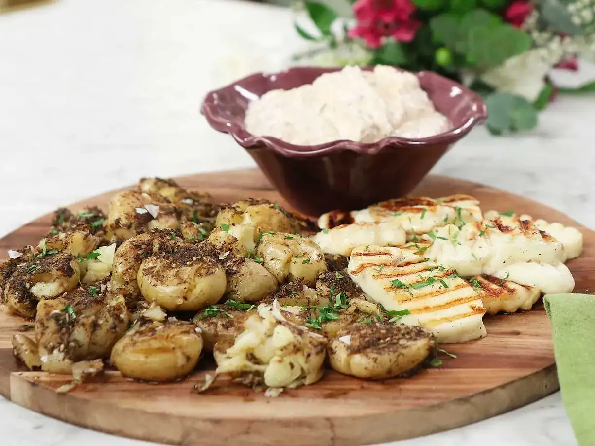 Smashed potatoes med kryddig sås till, bredvid grillad halloumi på en träbricka.