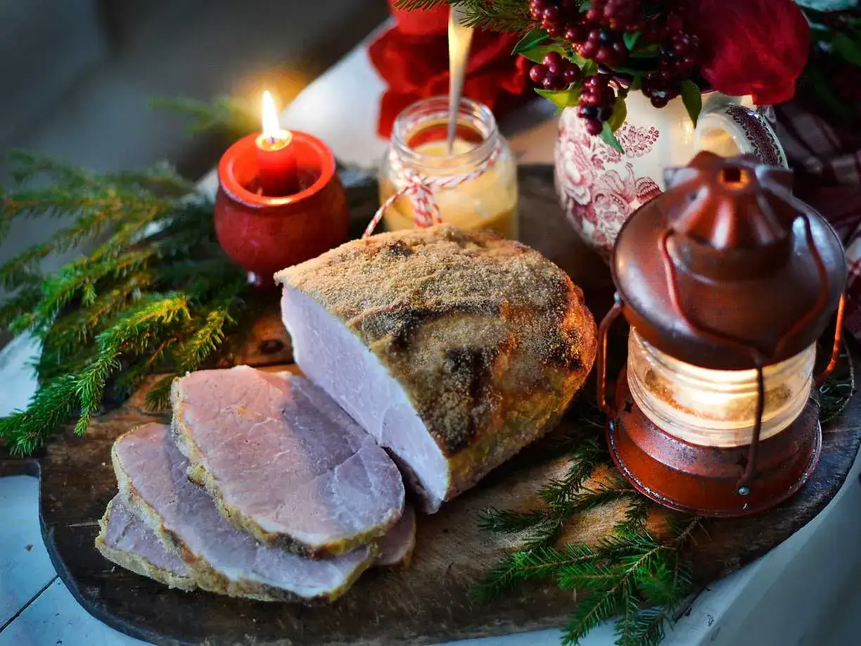En härlig griljerad skinka i ugn, uppskuren och redo att serveras. Julstämning med ljus, granris och en gammaldags lykta.