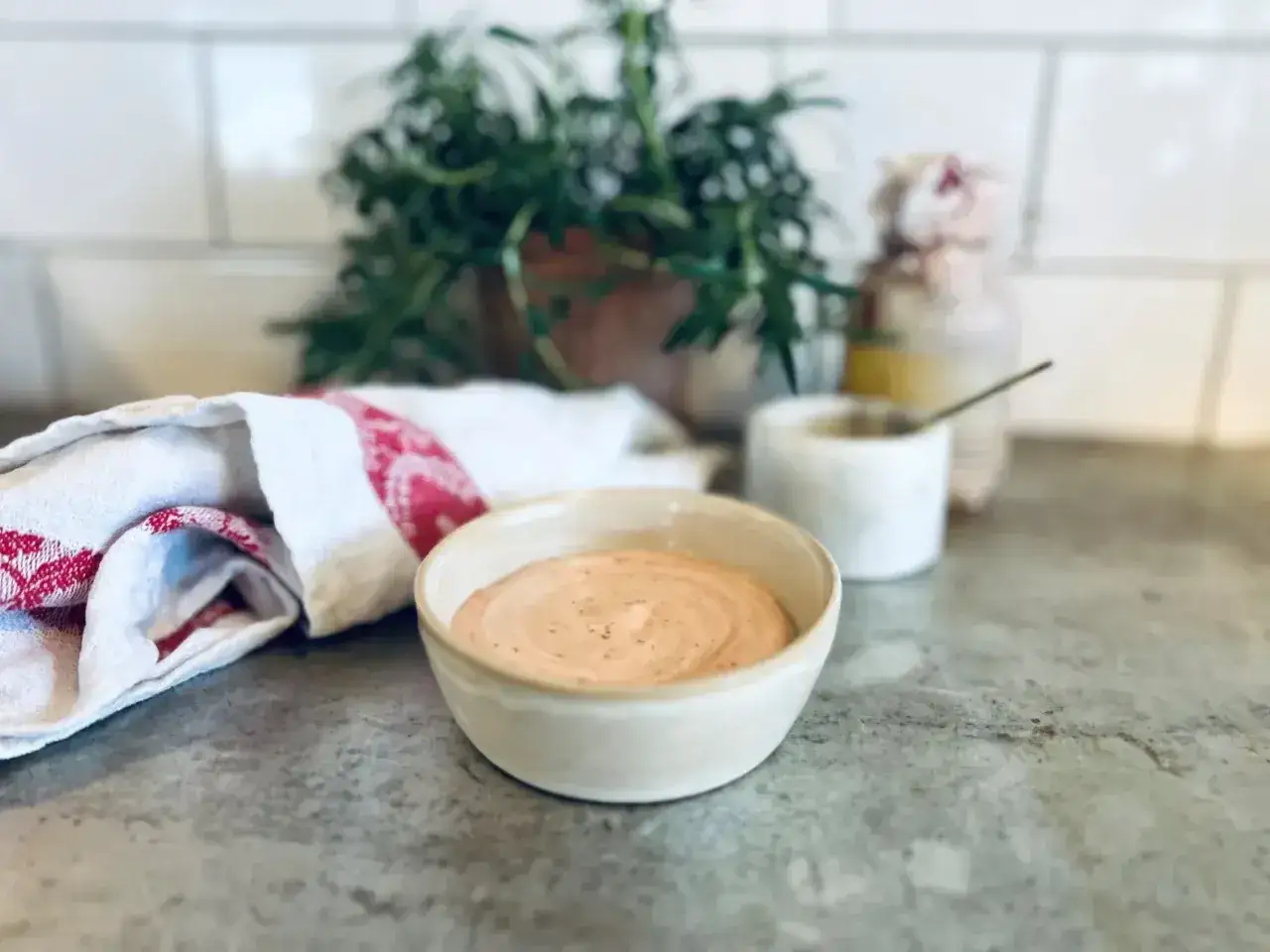 En skål med krämig Rhode Island-sås, perfekt för ditt nästa recept. En kökshandduk och grönska i bakgrunden.