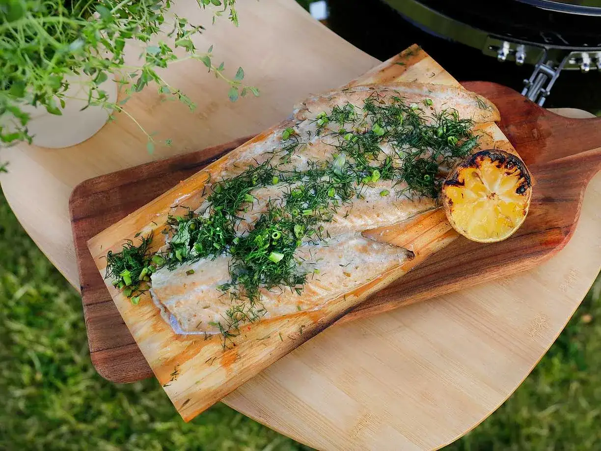 Stekt makrill på en träplanka, toppad med färska örter och en grillad citronklyfta. Perfekt för en sommarmåltid utomhus.
