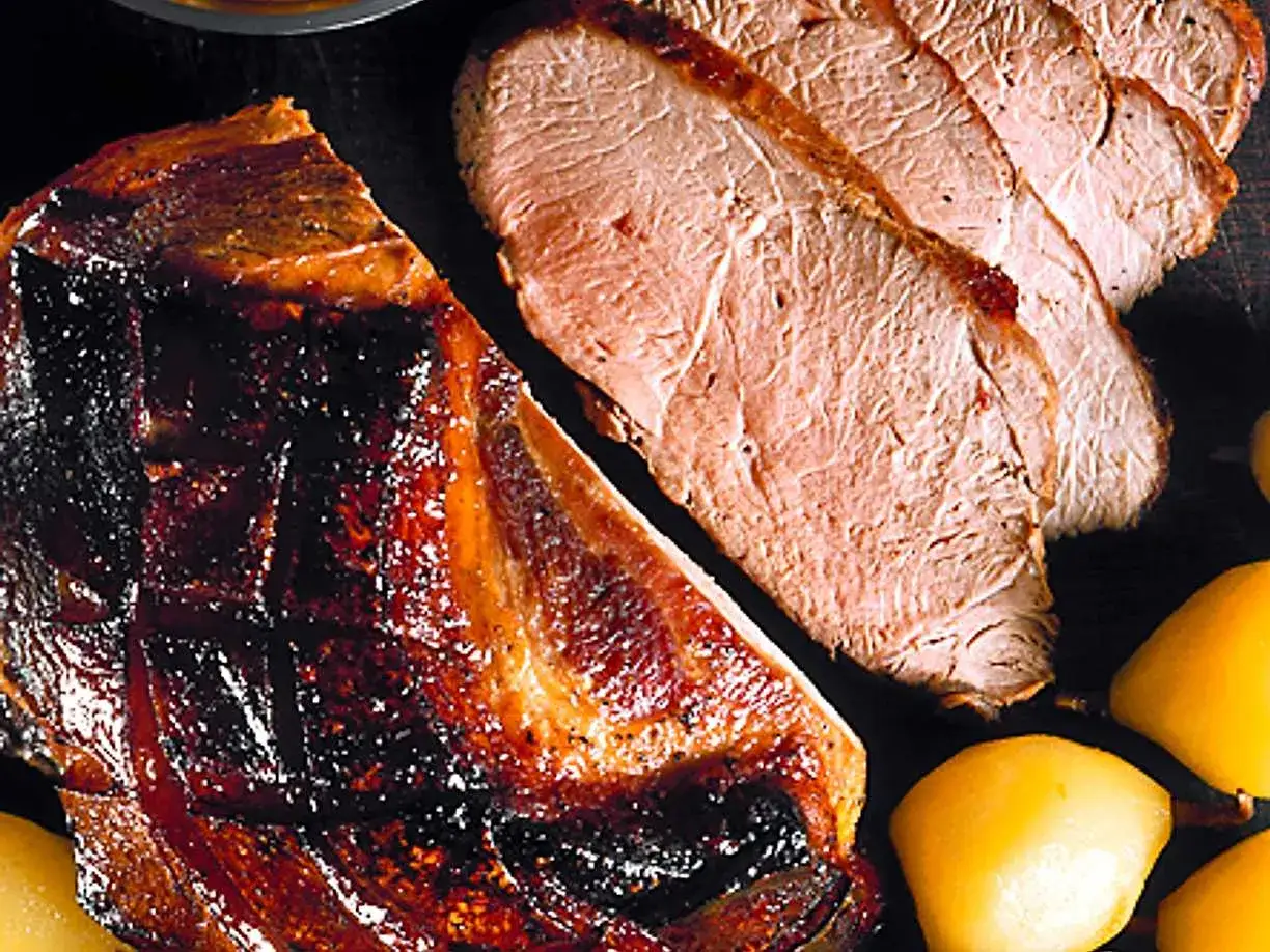 En saftig skinkstek med perfekt skinkstek temperatur, skuren i skivor bredvid glaserade p&auml;ron.