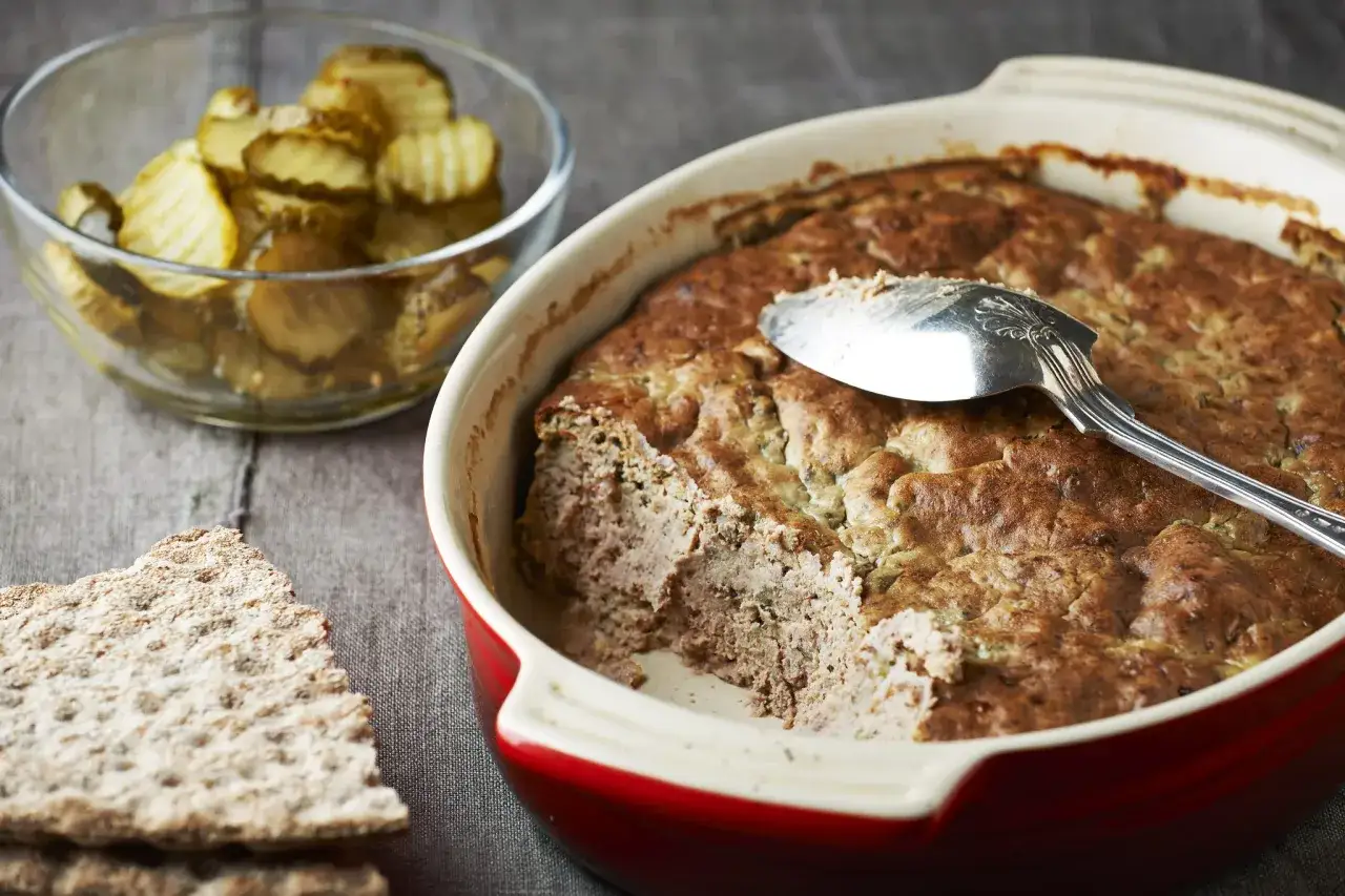 Här är ett läckert leverpastej recept! En ugnsform med nybakad leverpastej, skivad gurka och knäckebröd.