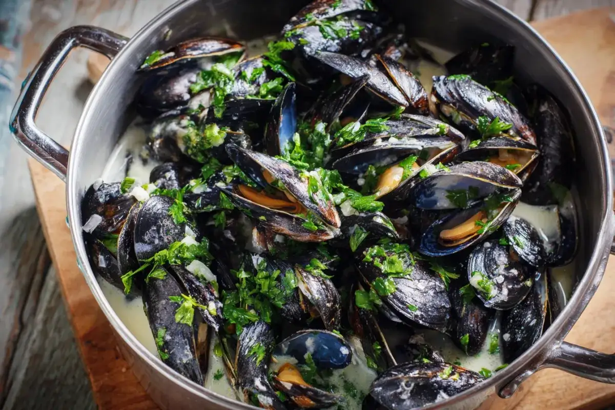 En stor gryta med &aring;ngande moules marini&egrave;res, toppad med f&auml;rsk persilja och vitl&ouml;k i en kr&auml;mig s&aring;s.