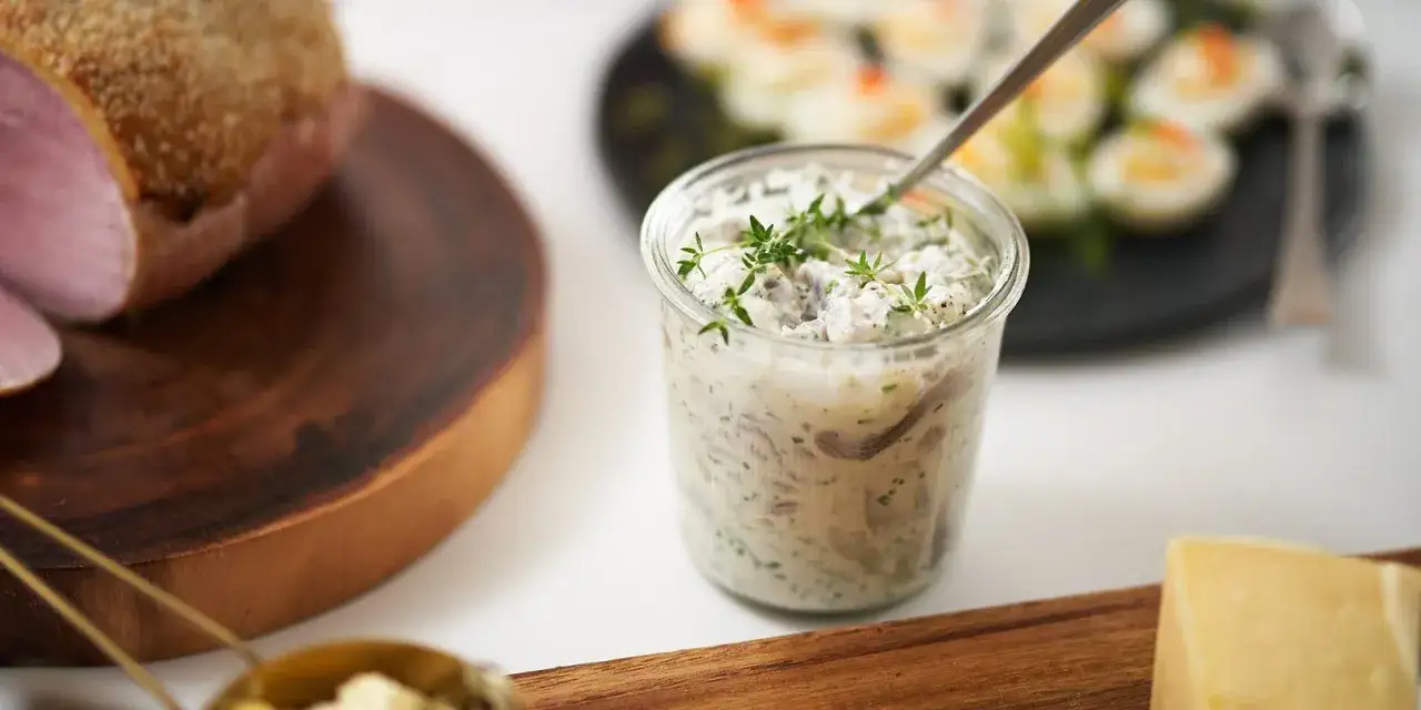 En burk med kr&auml;mig wasabi sill, toppad med f&auml;rska &ouml;rter. Bredvid syns en bit r&ouml;kt k&ouml;tt och ost.