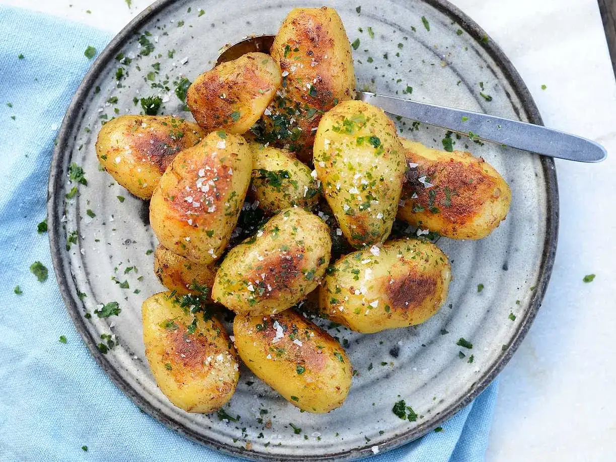 En tallrik med nykokta, gyllene sm&aring;potatisar, str&ouml;dda med flingsalt och f&auml;rsk persilja. Perfekt koka potatis tid!