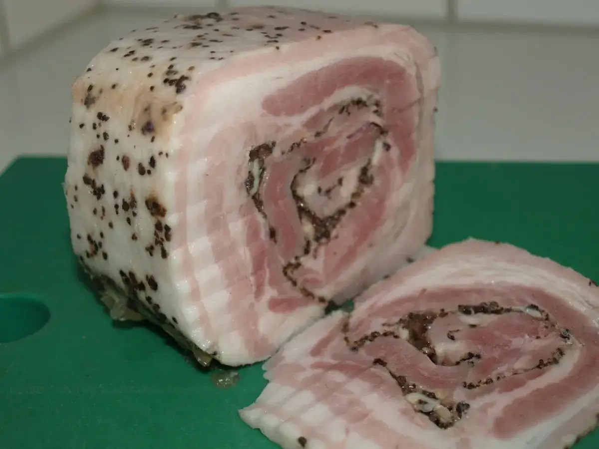 Rullsylta recept: en rulle av fl&auml;sk med lager av fett och k&ouml;tt, kryddad med peppar. En skiva ligger bredvid.