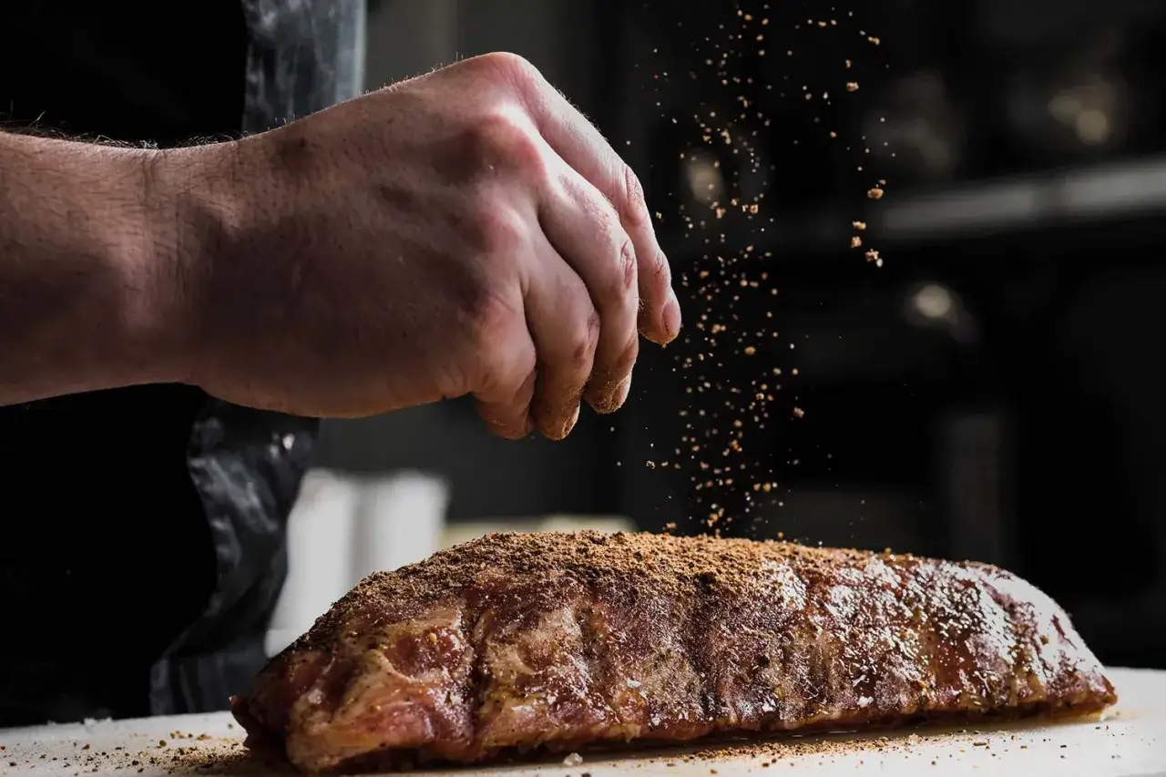 En hand str&ouml;r kryddor &ouml;ver en r&aring; flintastek. Perfekt f&ouml;r att uppn&aring; r&auml;tt temperatur vid grillning.