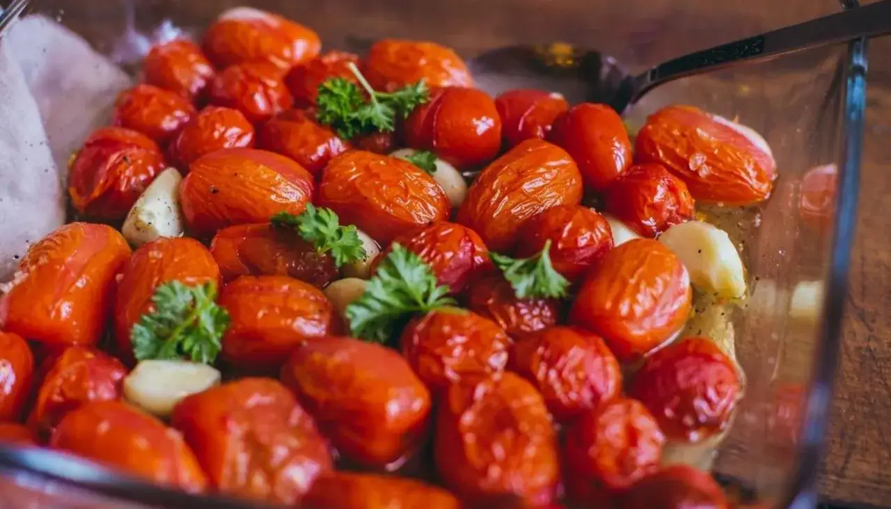 En glasform fylld med ugnsrostade k&ouml;rsb&auml;rstomater och vitl&ouml;k, garnerad med persilja. Perfekt f&ouml;r en smakrik rostad tomats&aring;s.