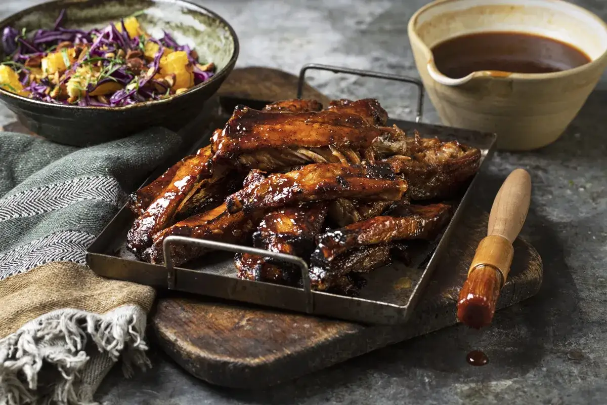 Glacerade spareribs i ugn, redo att serveras med en fr&auml;sch k&aring;lsallad och en sk&aring;l med s&aring;s.